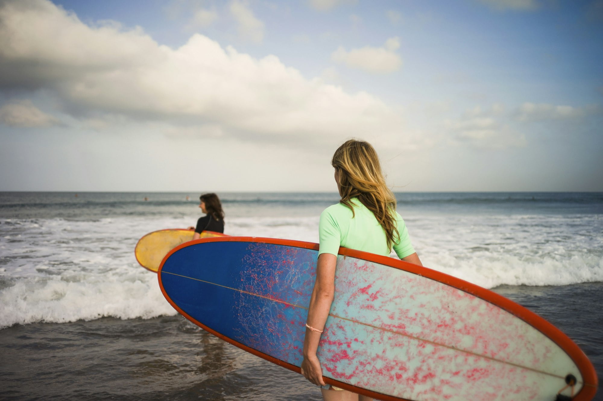 Two woman walking out to sea, carrying surfboards, Seminyak, Bali, Indonesia